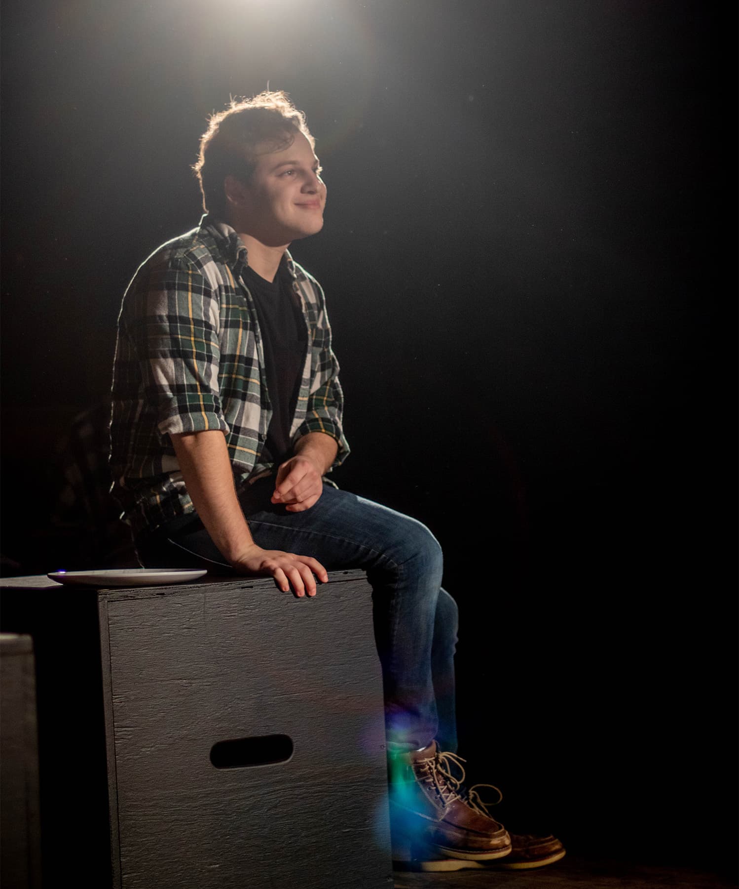 Jacob sitting on a wooden box, smiling, wearing green flannel.